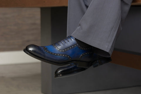 Person wearing blue dress shoes and gray pants sitting on a bench.